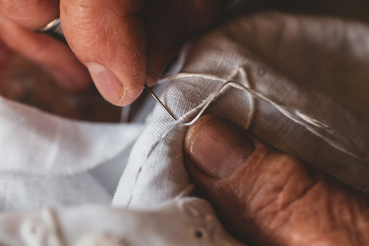 Mãos de artesão a coser um estofo à mão